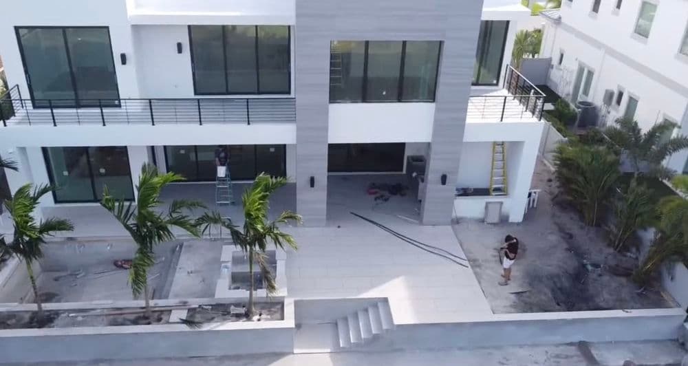Aerial view of a modern house under construction with landscaping and workers present.