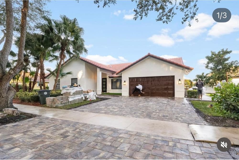 Modern home exterior with brick driveway, palm trees, and landscaping in sunny environment.