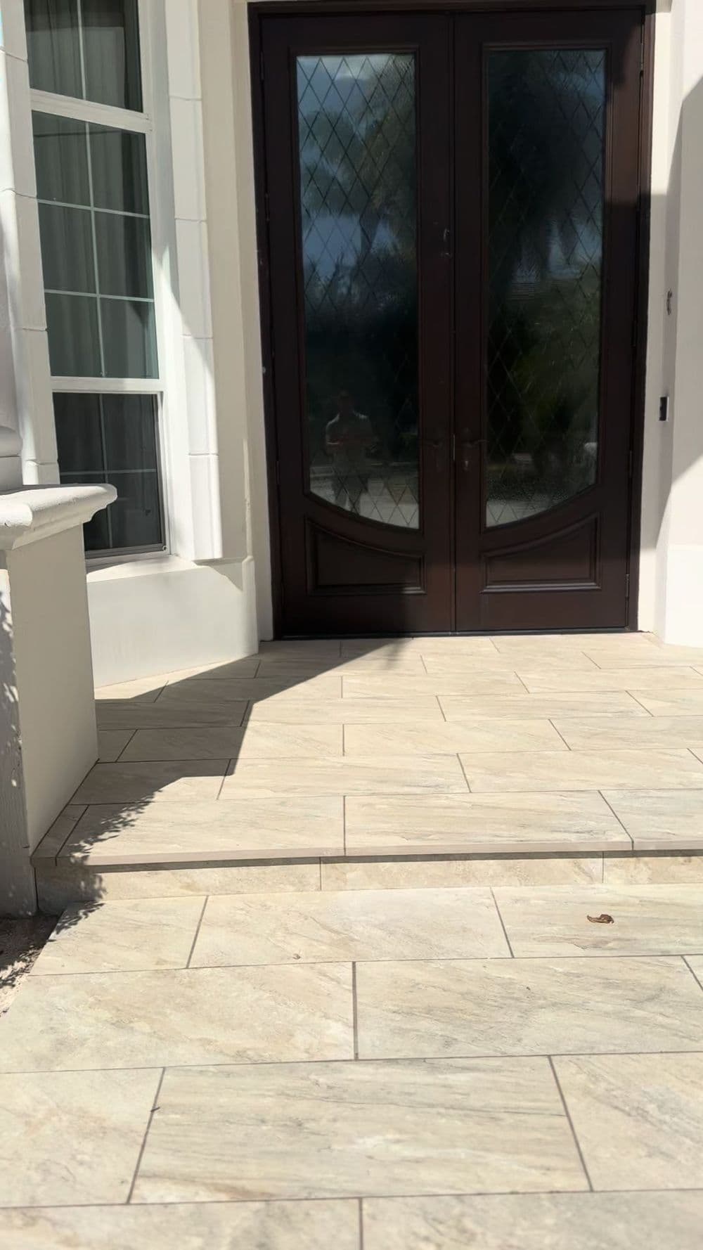 Elegant front entrance with double doors and patterned stone steps, featuring sunlight shadows.