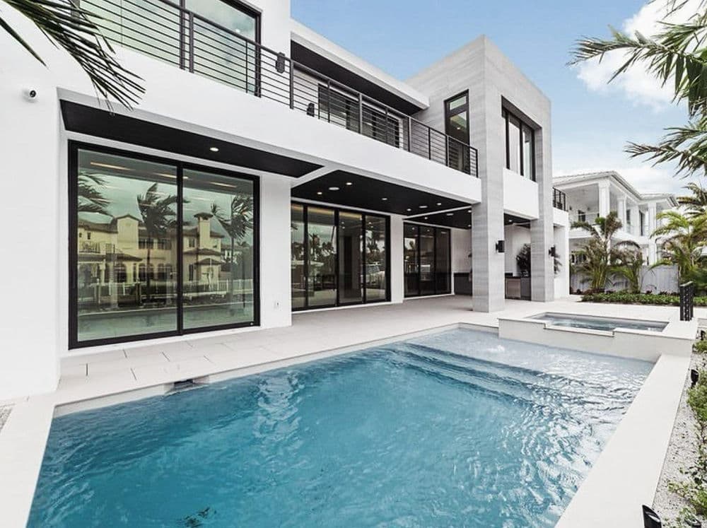 Modern luxury home with a pool, large windows, and palm trees in a sunny setting.
