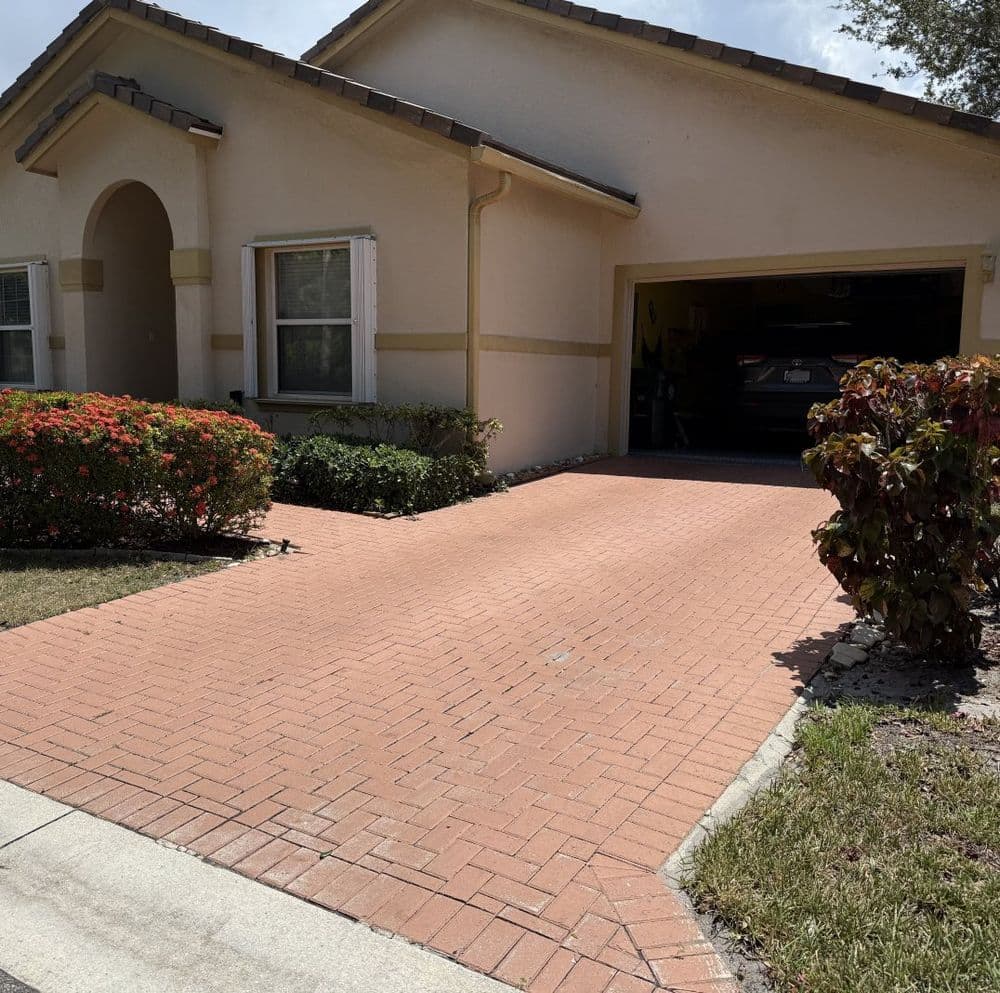 Brick driveway leading to residential home with landscaped garden and garage.