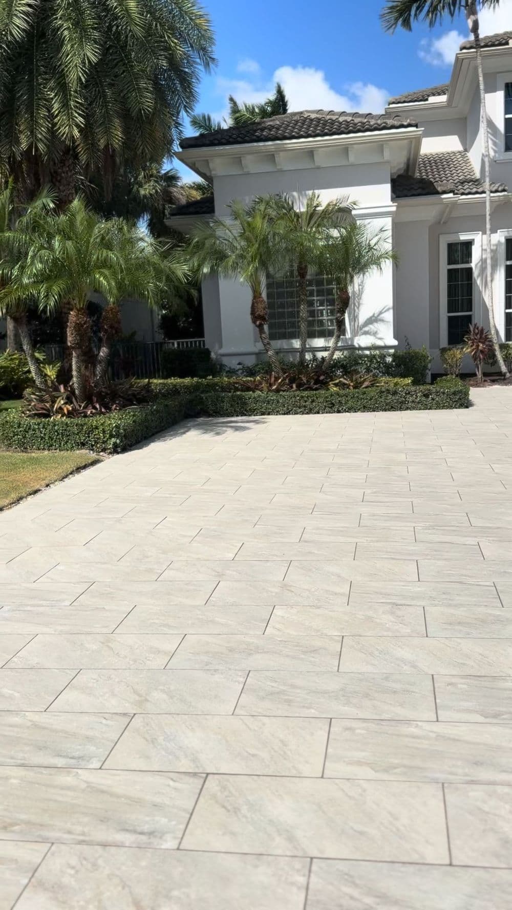 Elegant home exterior with a marble tile driveway and tropical landscaping. Palm trees in view.