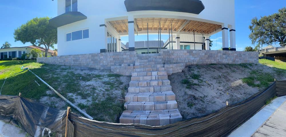 Newly constructed home with stone steps leading to a spacious patio area on a sunny day.