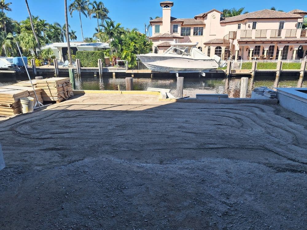 Vacant waterfront lot prepared with sand and gravel, boats in the background, sunny day.
