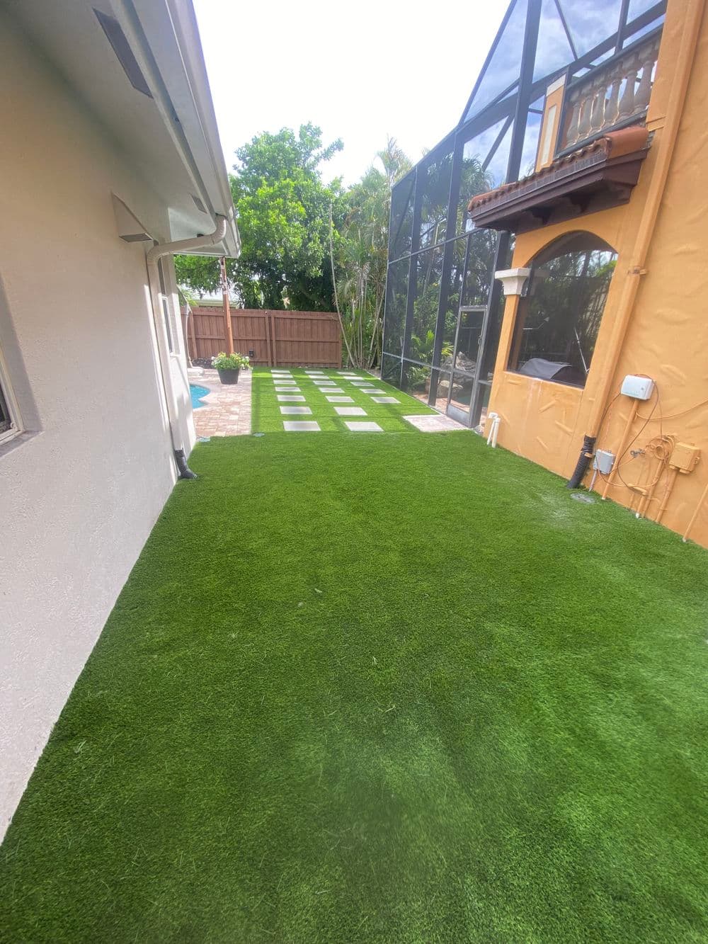 Lush artificial grass backyard with paver pathway and spacious patio area.