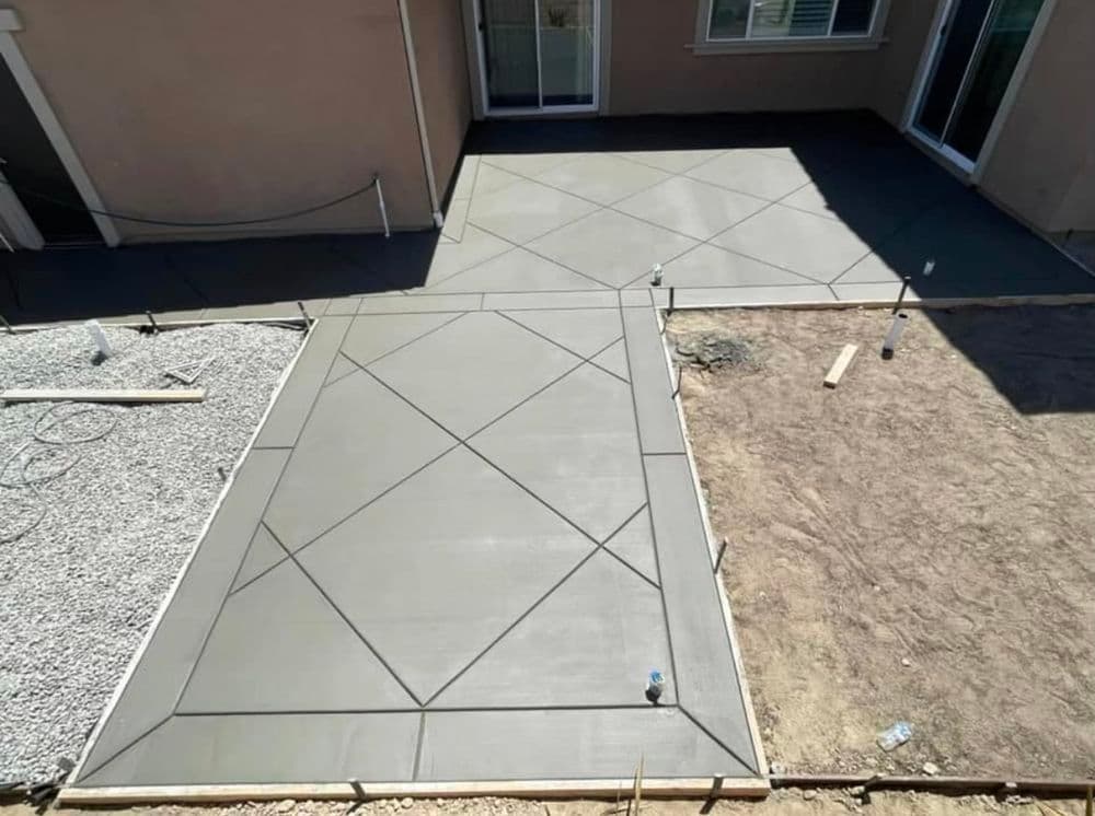 Newly poured concrete patio with decorative pattern next to gravel and dirt areas.