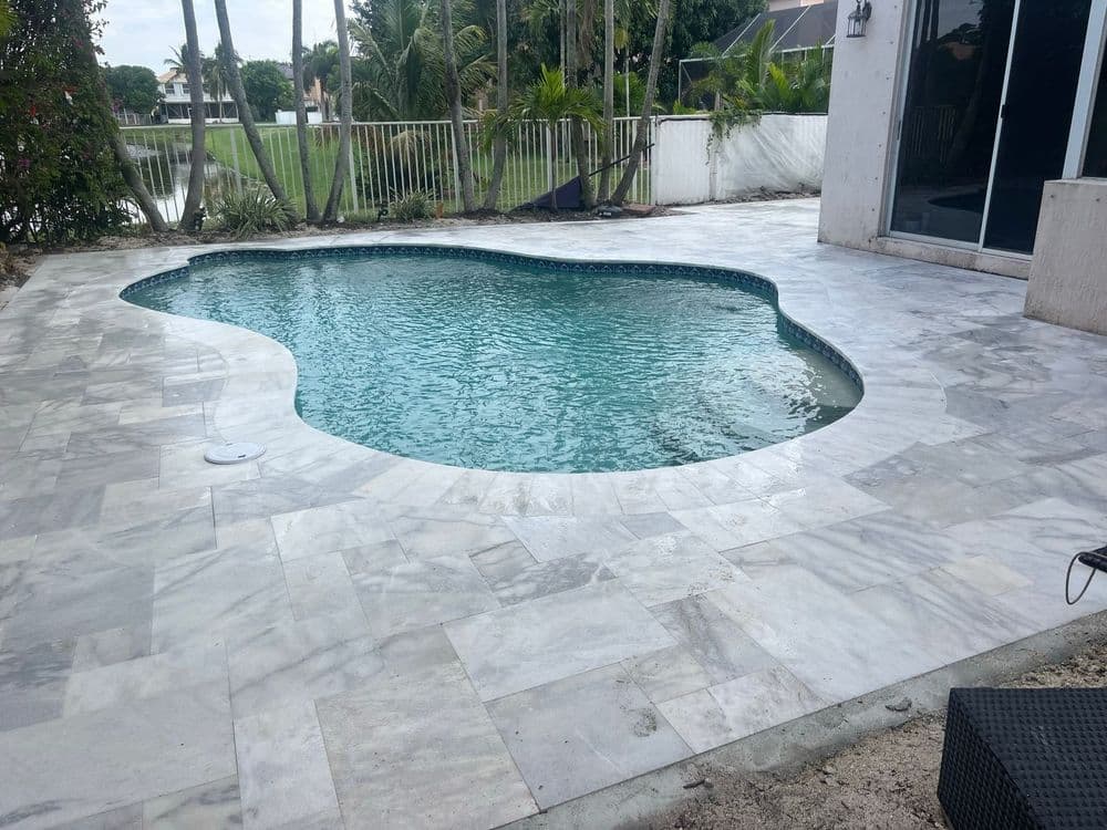 Elegant backyard pool with a unique shape surrounded by marble flooring and lush greenery.