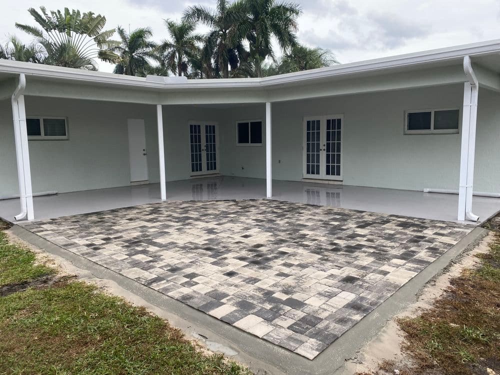 Modern home exterior with a spacious patio and paver landscaping, surrounded by tropical vegetation.