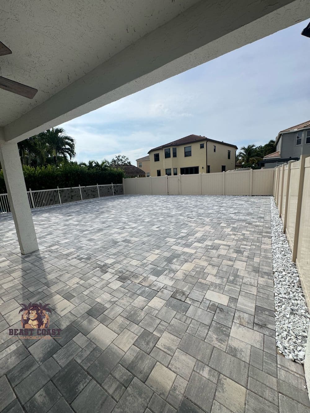 Spacious outdoor patio with paved stones and fenced backyard under a clear sky.