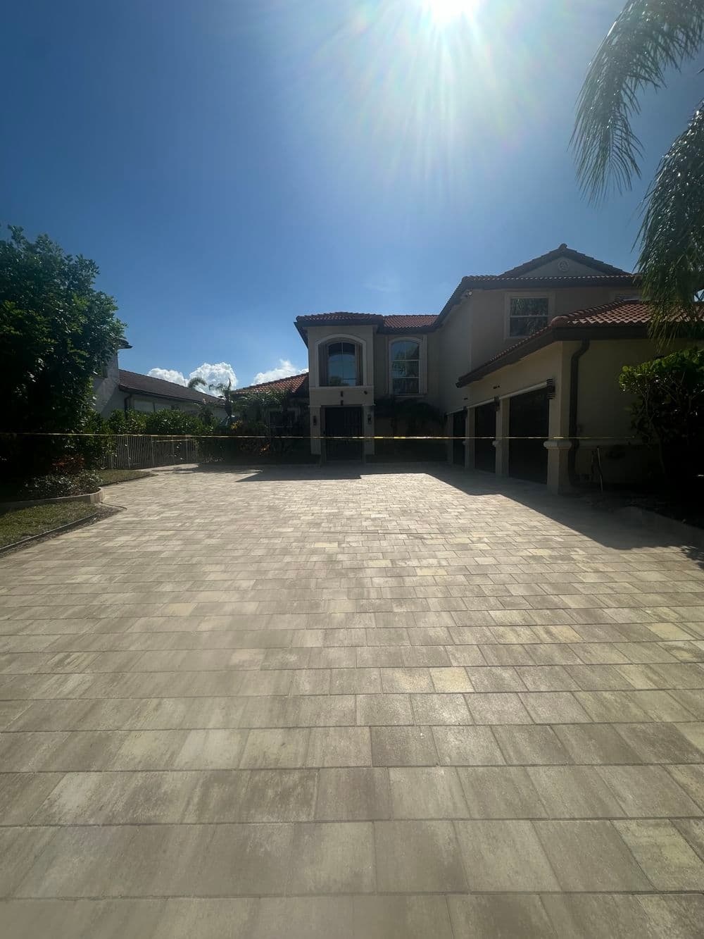 Luxury home exterior with a spacious driveway, clear blue sky, and tropical landscaping.