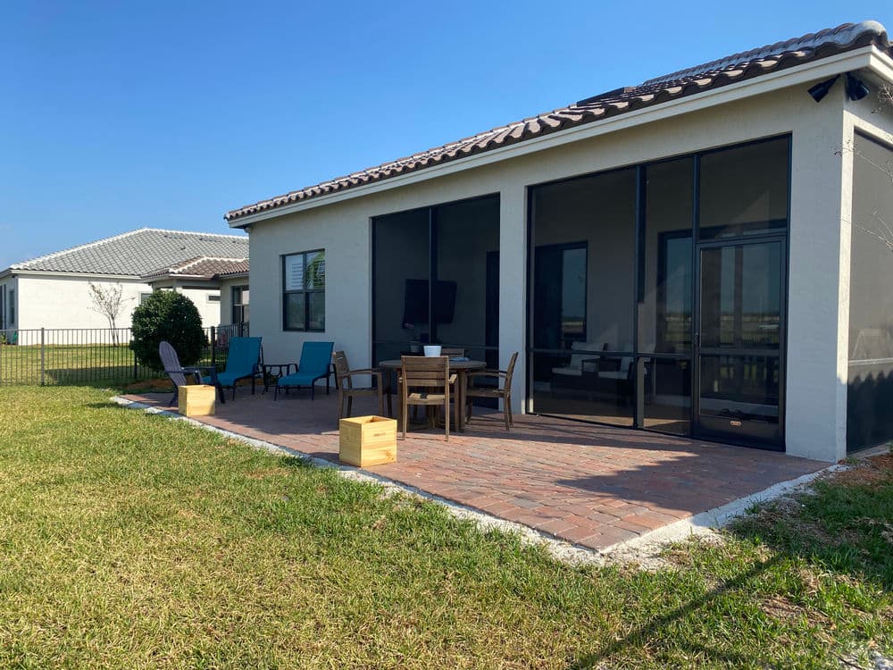 Patio with seating area and glass door in modern home, surrounded by grass and blue sky.
