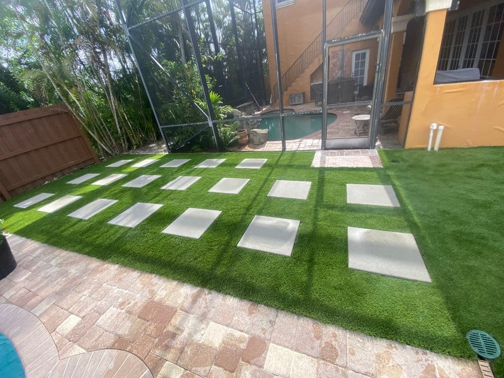 Modern backyard with artificial grass, stepping stones, and a pool visible through a screen enclosure.