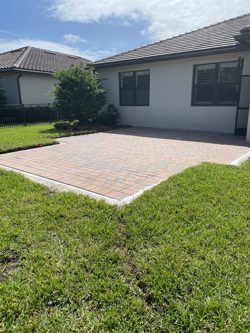 Paved outdoor patio area with grass borders and modern home in the background.