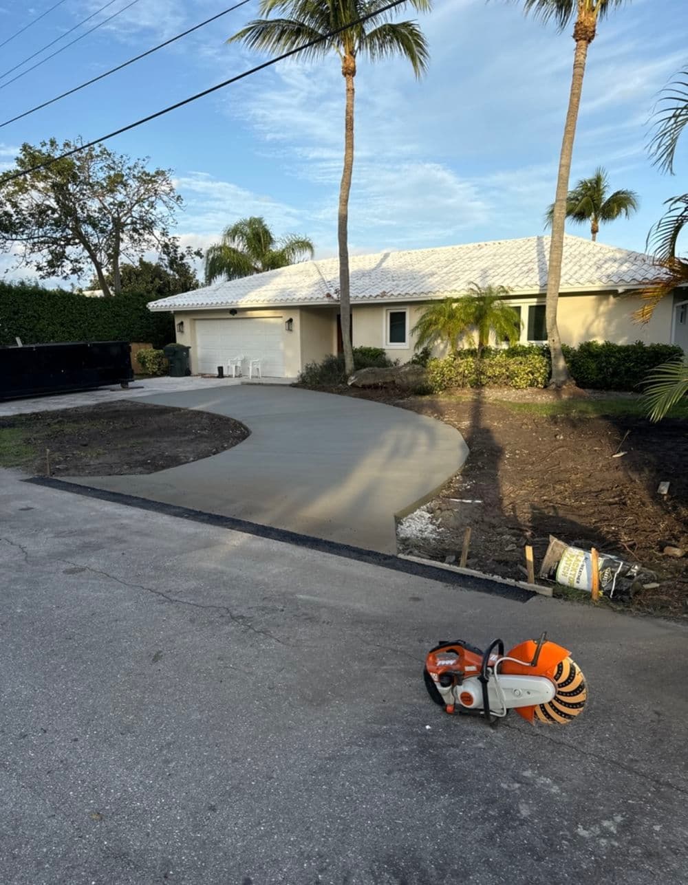 Freshly poured concrete driveway near a home with palm trees and construction equipment visible.