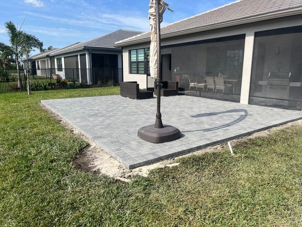 Paved patio area with an umbrella stand and green lawn in a residential backyard.