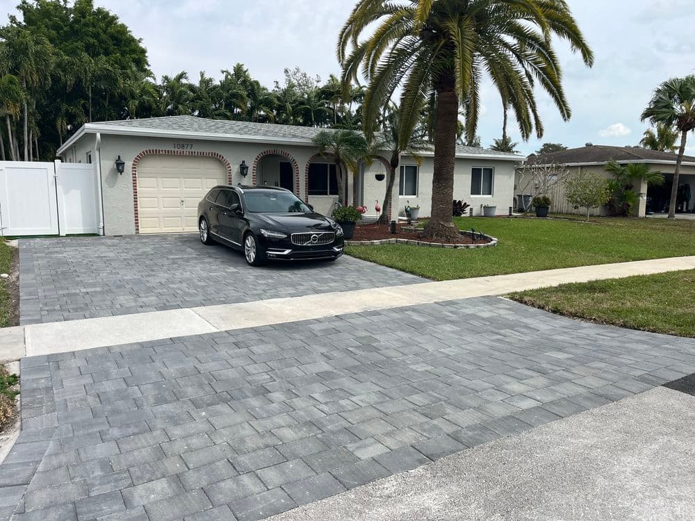 Modern home with a black car parked on a paved driveway surrounded by tropical landscaping.