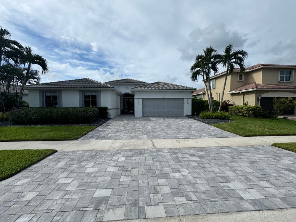 Modern single-story home with a paver driveway and lush landscaping under a cloudy sky.