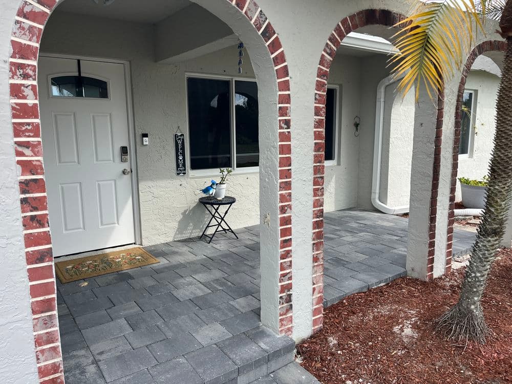 Brick-arched entrance with a paver walkway leading to a front door and palm tree.