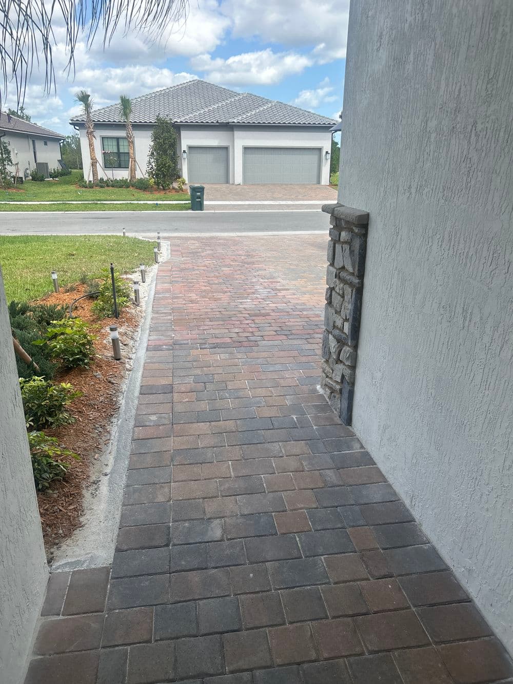 Paver walkway leading to a house with a landscaped front yard and two-car garage.
