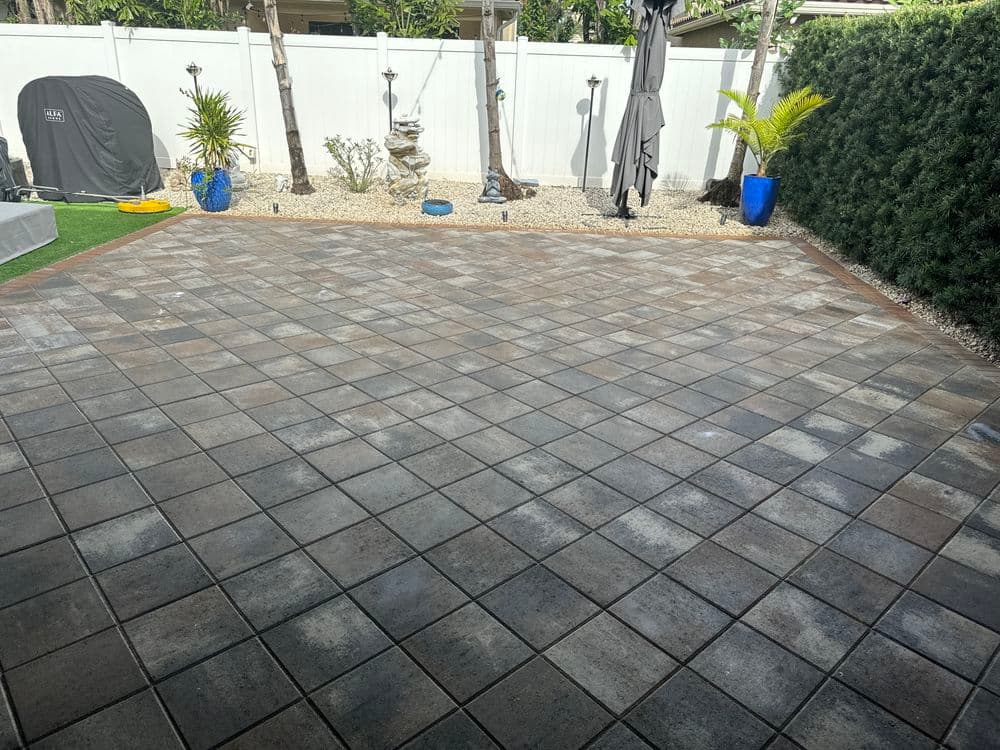 Paved outdoor patio with patterned tiles, tropical plants, and a shaded area for relaxation.