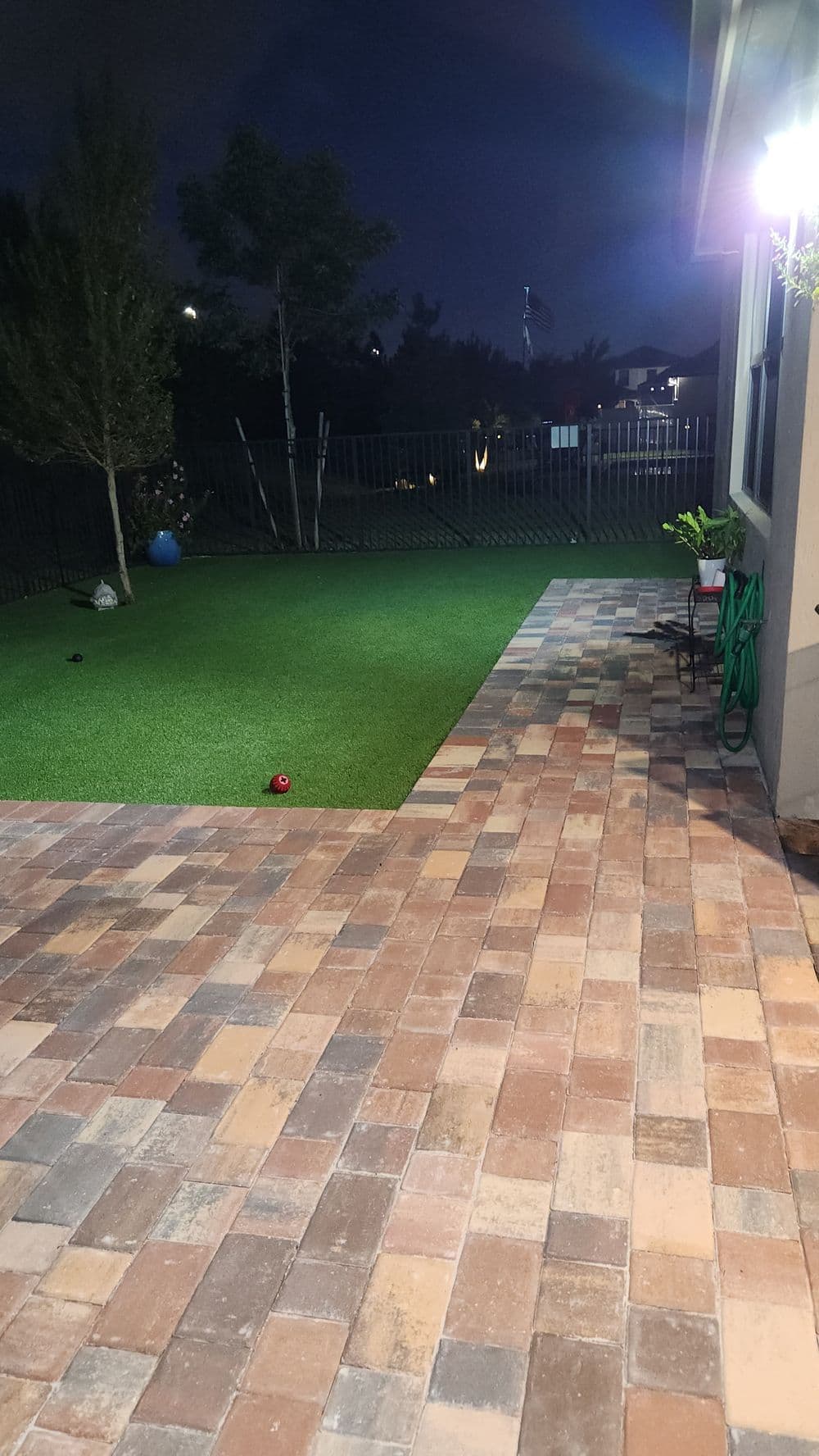Nighttime backyard view featuring a green lawn, paver stones, and decorative plants.