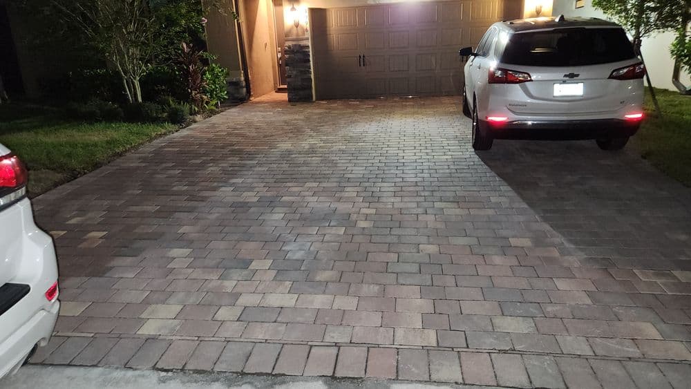 Paved driveway with two parked cars and a garage in a well-lit residential area.
