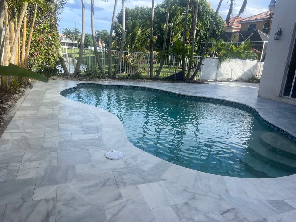 Luxury backyard with a sparkling pool surrounded by palm trees and elegant marble paving.