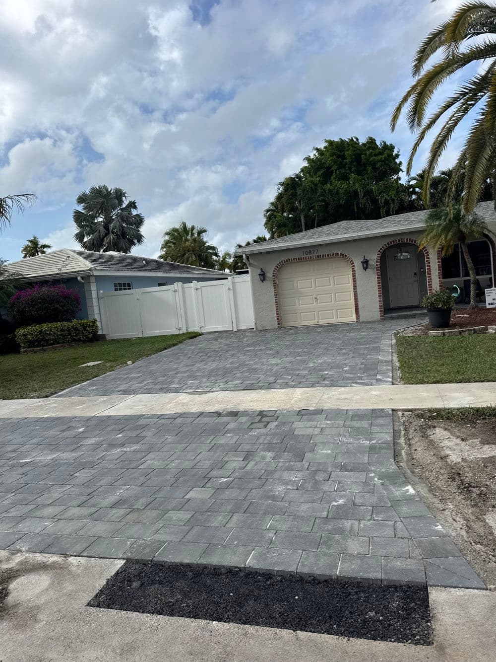 Paver driveway and beautiful home in a sunny residential area with palm trees and lush landscaping.