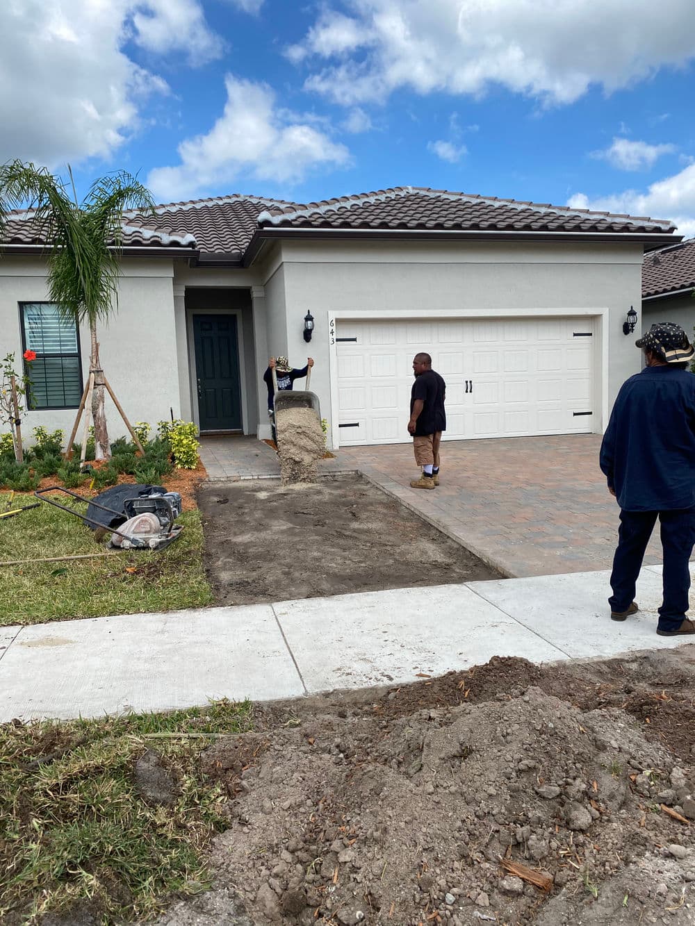 Workers landscaping in front of a new home with a paved driveway and cloudy sky.