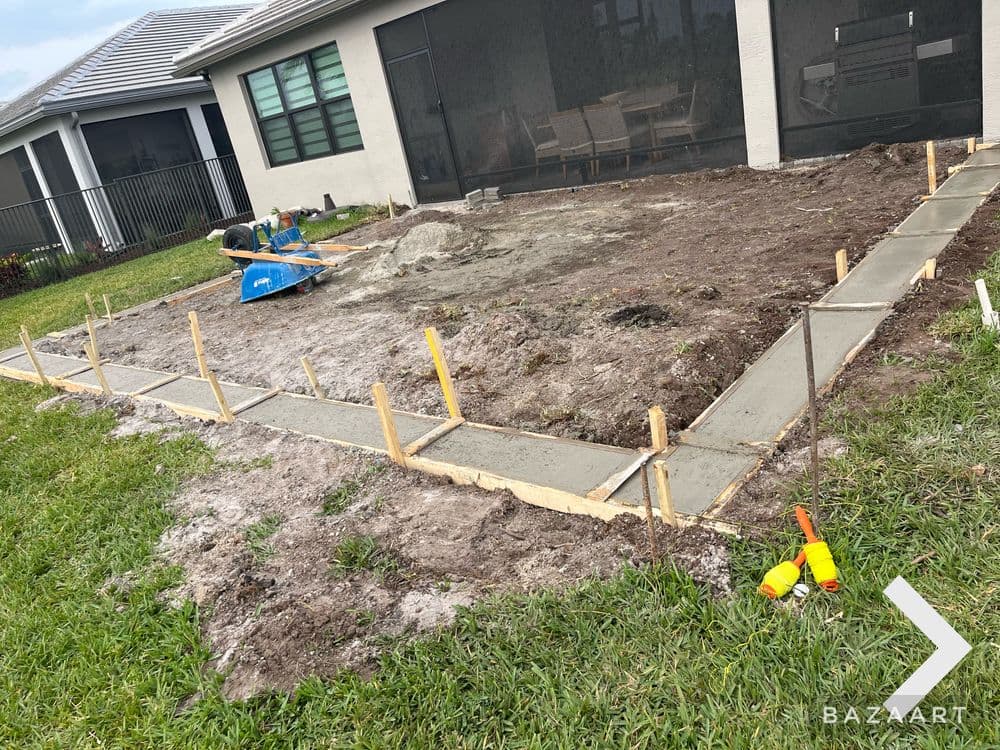 Construction site with freshly poured concrete and wooden frames for a patio extension.