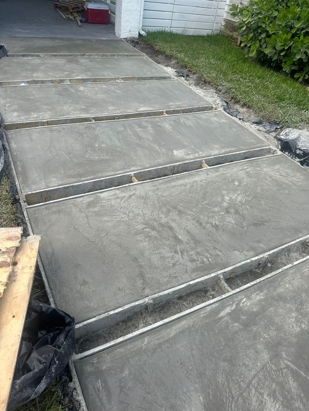Freshly poured concrete driveway sections with wooden forms, surrounded by grass and landscaping.