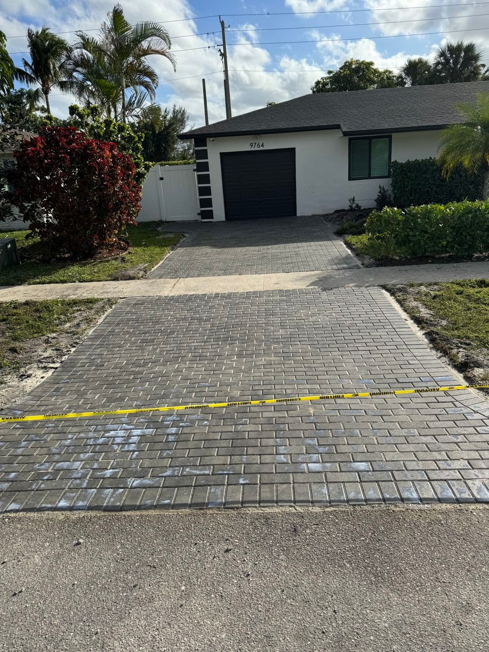 Paved driveway in front of modern house with lush landscaping and clear blue sky.