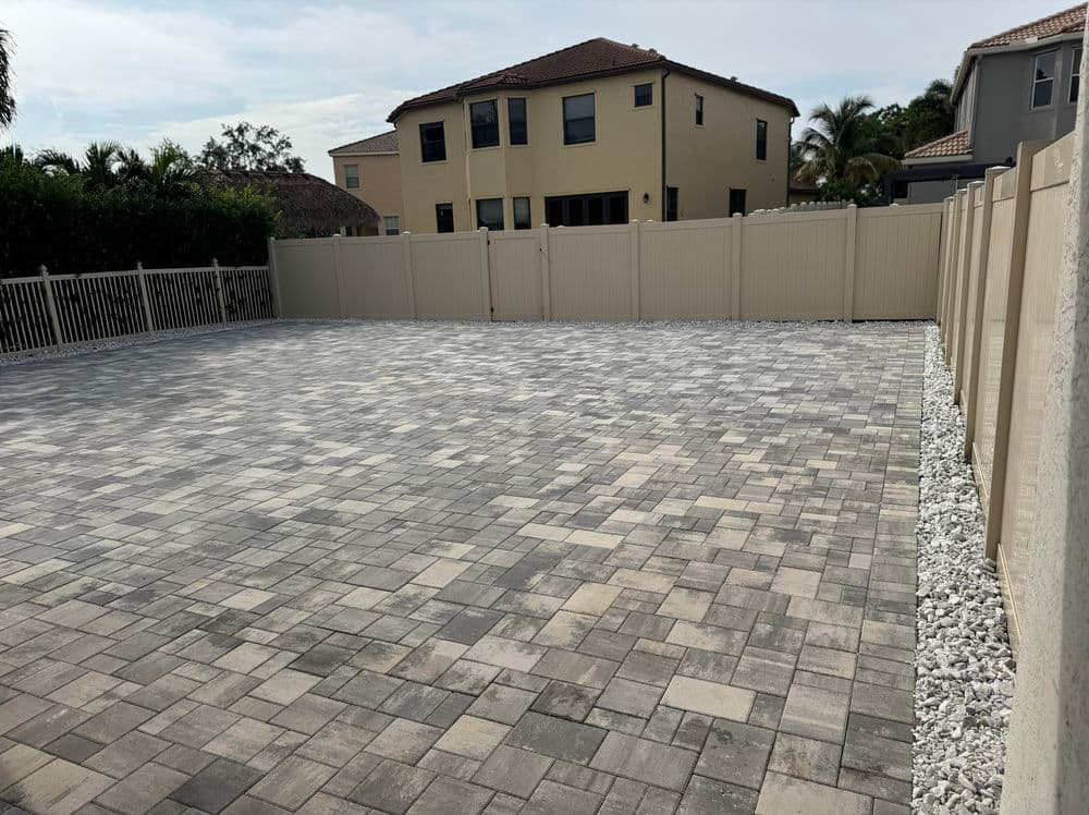 Paved outdoor space with light gray stones and surrounding beige fence in residential area.